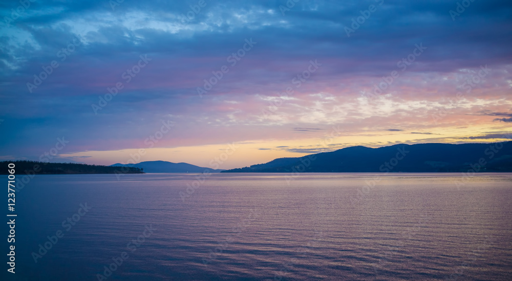 Pink and orange sunset over hills and water in Tasmania, Australia.