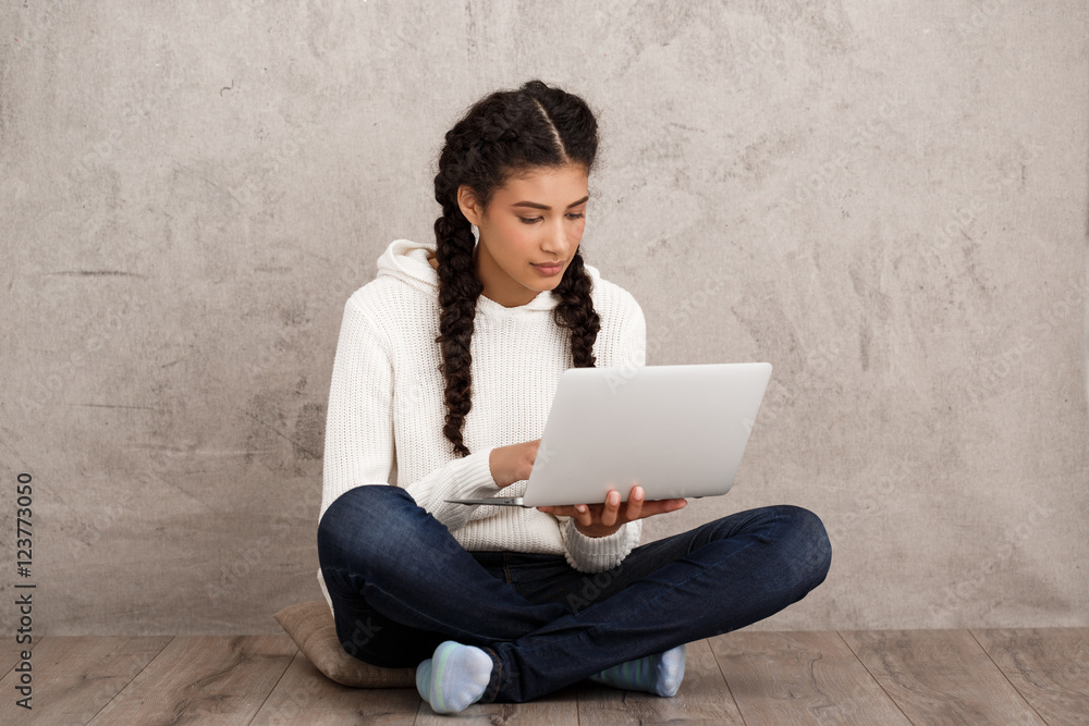 Girl smiling, holding laptop, sitting on floor over beige background. Girl smiling, holding laptop, sitting on floor over beige background.