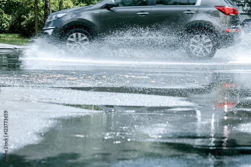 city road after rain. black car driving through rain puddle and reflecting in it.