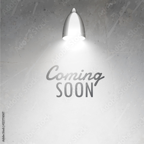 coming soon text placed under glowing lamp on gray textured wall