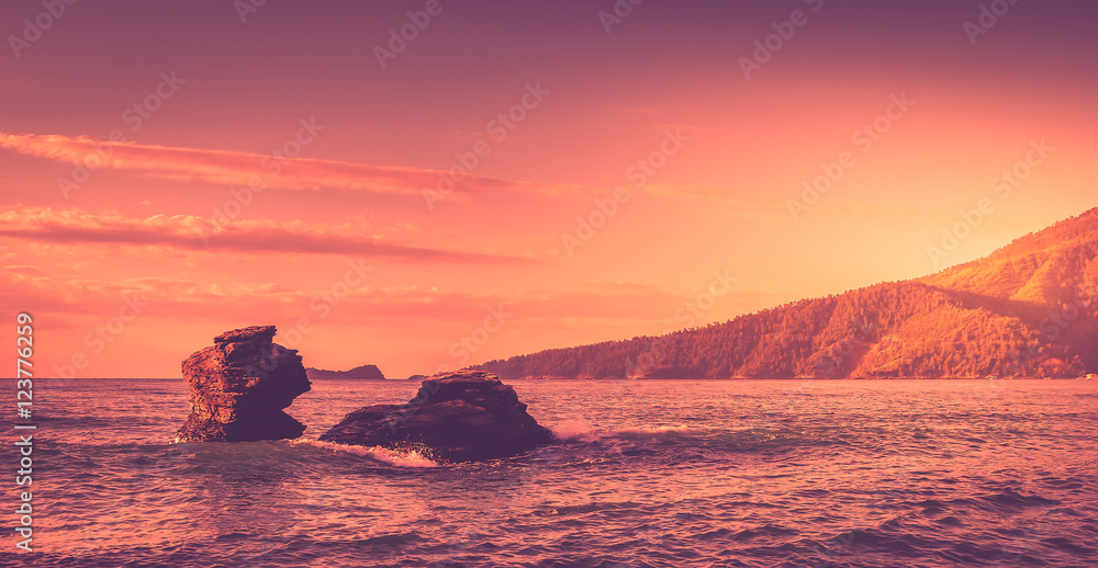 Sunrise scene at the sea. There are two cliffs into the water.