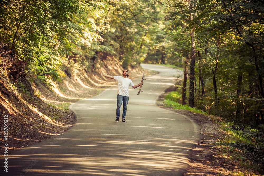 Fototapeta premium Skateboarder standing in the middle of the road in the forest and raising his hands up