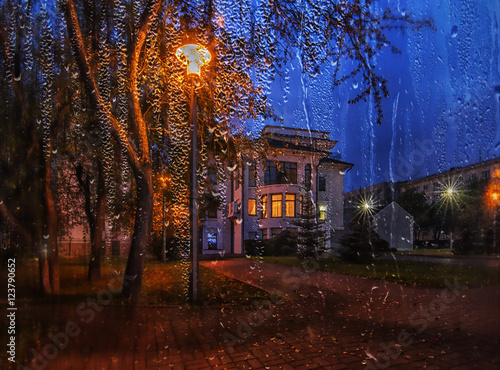 Landscape with house in raining night through the wet window
