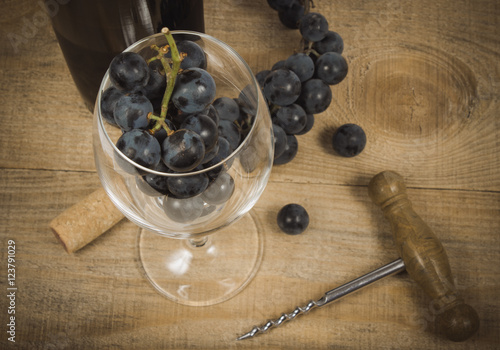 Glass of red wine with a sprig of grapes on a wooden table.