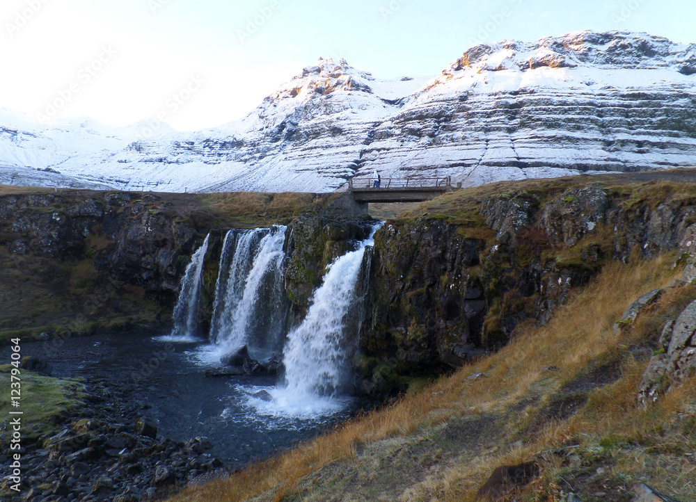 Fototapeta premium Kirkjufellsfoss waterfall and the snow capped mountain in the morning sunlight, Snaefellsness Peninsula of Iceland