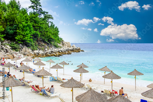 Marble beach (Saliara beach), Thassos Islands, Greece. The most beautiful white beach in Greece. Tourists enjoying a nice day at the beach. Straw umbrellas (straw parasol) and sunbeds on the beach. photo