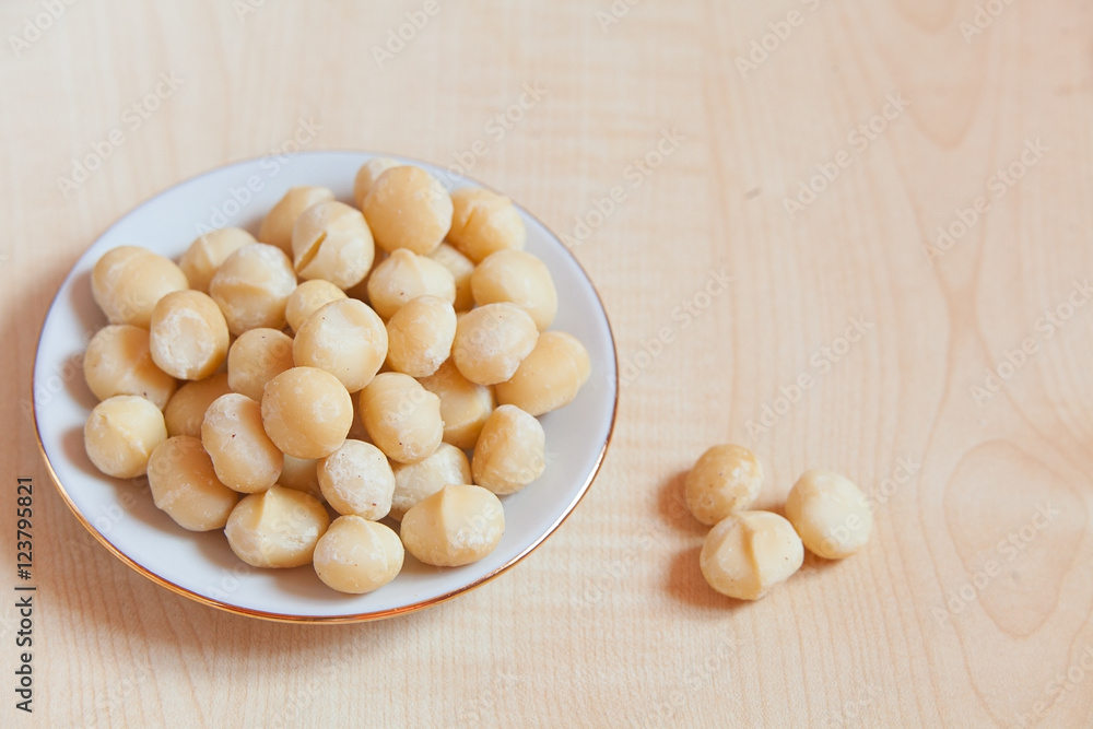 delicious macadamia nuts on  plate on  wooden background