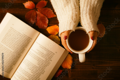 Woman hands holding teacup and opened book seen from above