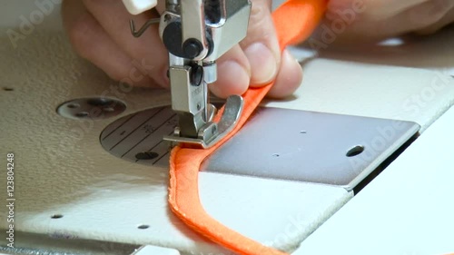 Seamstress Stretch Material, Stitching Strip, Using Sewing Machine. Red Fabric Under the Needle. Bright Light, Neat Work. Closeup photo