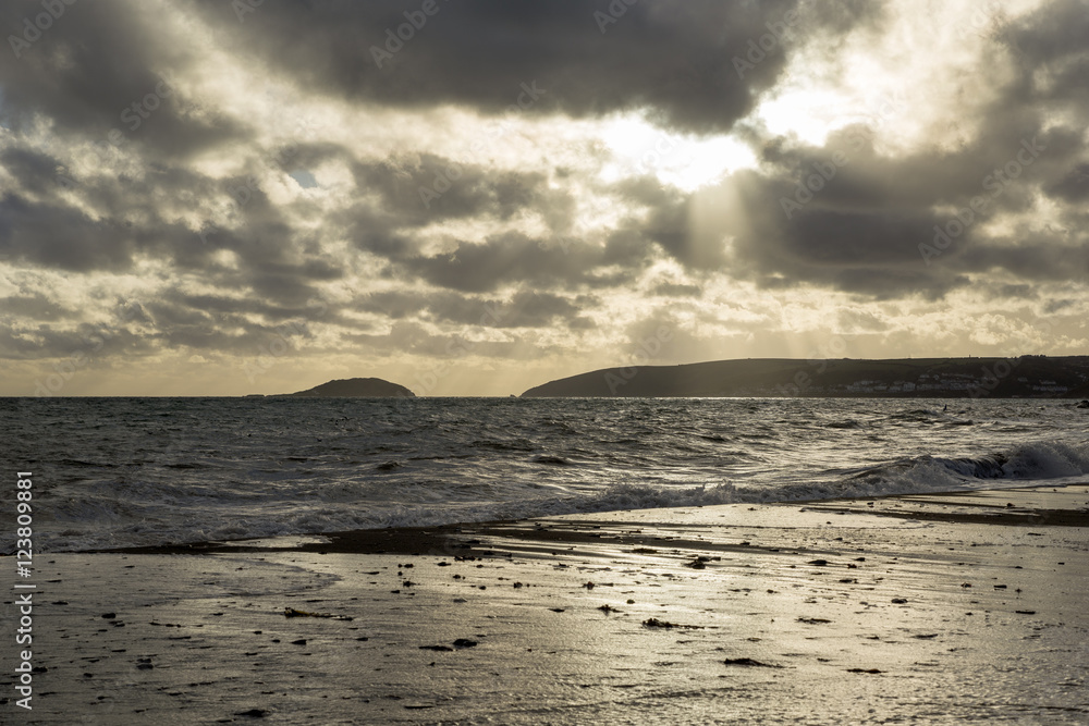 Stormy sunset at Seaton with cloudy sky and waves in the ocean, Cornwall, UK