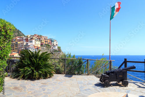 Old cannon, Italian flag and Cinque Terre village Manarola with colorful houses and Mediterranean Sea, Italy
