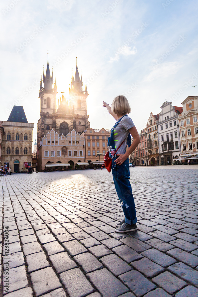 Fototapeta premium Beautiful young woman points to the Church of Virgin Mary in Old Town Square in Prague. Kostel Panny Marie pred Tynem.