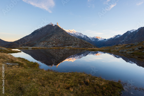 High altitude alpine lake in idyllic land with reflection of majestic rocky mountain peaks glowing at sunset. Wide angle view on the Alps. © fabio lamanna