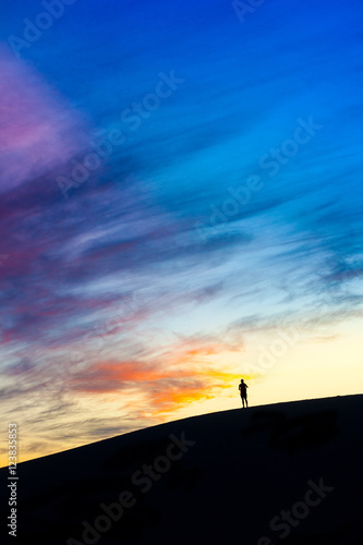 A man travelling alone silhouette in windy white sand dunes with dramatic twilight evening sky at Muine desert, Phan thiet, Vietnam
