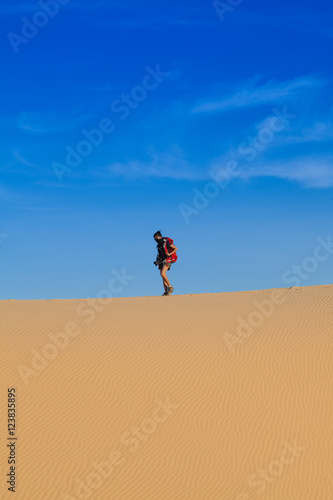 Female photographer with her backpack travelling in windy white sand dunes at Muine desert, Phan thiet, Vietnam