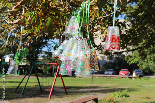 Recycle project of plastic bottles and cups, colored with different colors. Second life for plastic. Kids project in the backyard. Plastic hanging from the tree. Save environment.