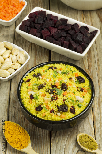 Vegetable couscous in a black bowl and ingredients on a wooden table