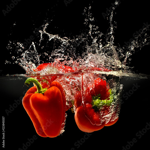 Group of bell pepper falling in water with splash on black background