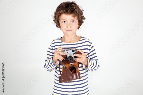  Cheerful smiling child (boy) holding a film camera over white 