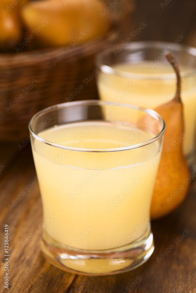 Birnensaft im Glas mit Bosc Birne im Hintergrund (Selektiver Fokus, Fokus auf die Vorderkante des Glasrandes)