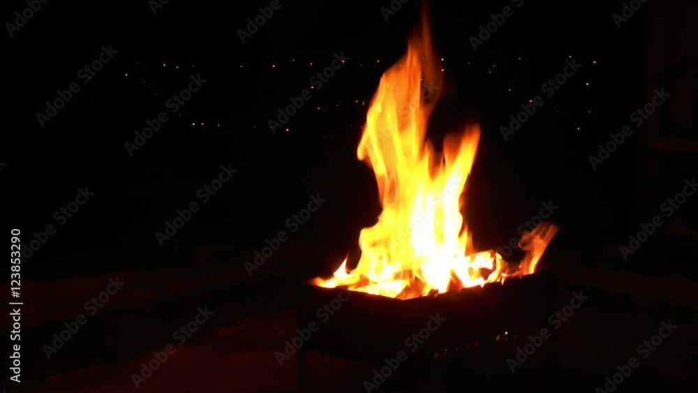 Lit the fire in the grill, in the background is shining garland. Sometimes falling snowflakes. Lit the fire in the grill, in the background is shining garland. Sometimes falling snowflakes.
