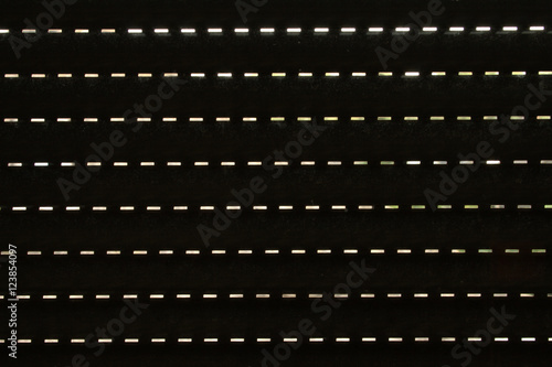 Small lit slits as seen from behind a window roller shutter, material texture