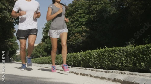 Sport couple running jogging in city park. Runners exercising - woman and man runner training on run living healthy active lifestyle in Retiro Park in Madrid, Spain, Europe. RED EPIC SLOW MOTION.