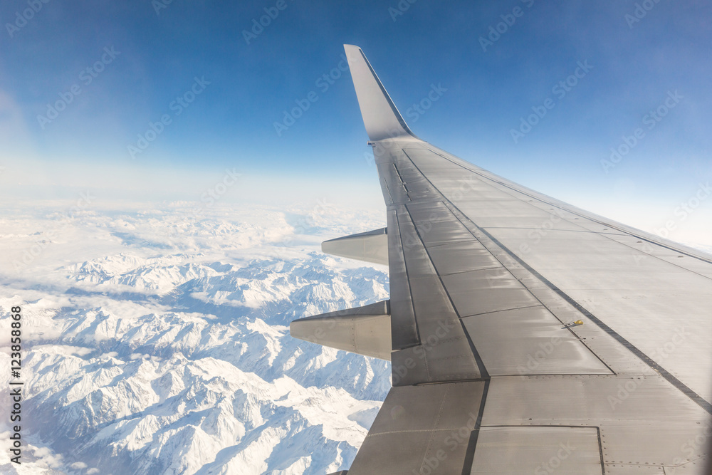 Airplane window seat view while flying over snowy mountains