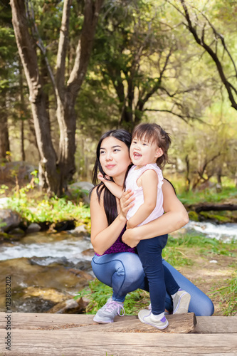 Asian Woman with her little daughter in the woods near the river standing on a log