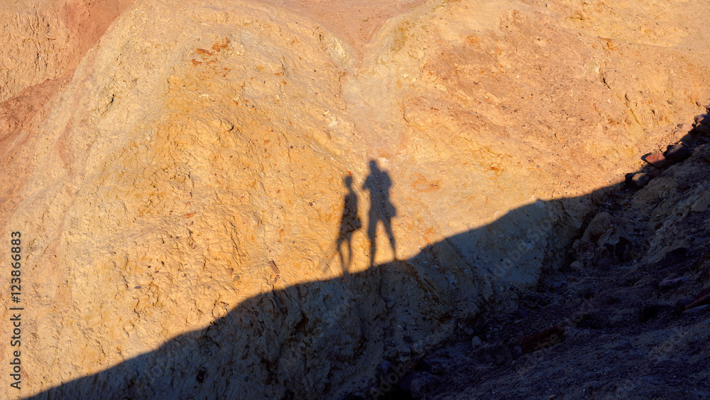 Two shadows of hikers silhouettes on a background of yellow mountains