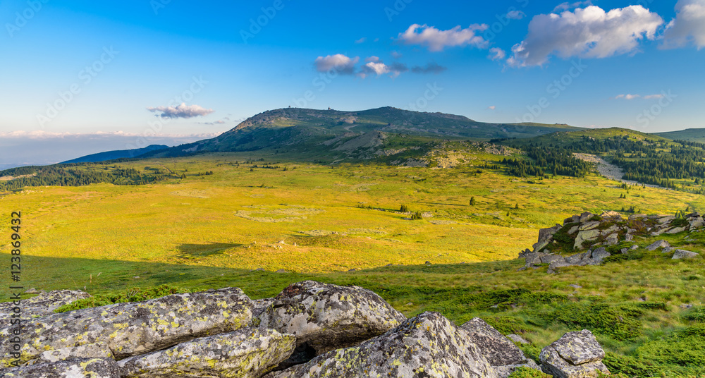 Gentle rays of sunlight over a vast mountain plateau at Vitosha, Sofia, Bulgaria - rocks in the foreground, beautifully lit meadow in the middle and Black Peak in the far background