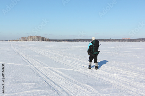 The man the traveler with a backpack skiing on snow cover of the river 