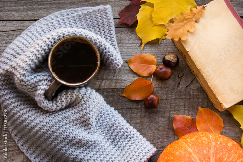 Mug of coffee, cozy knitted scarf, autumn leaves, open book and pumpkin on wooden board. Autumn still life, vintage style. Flat lay.
