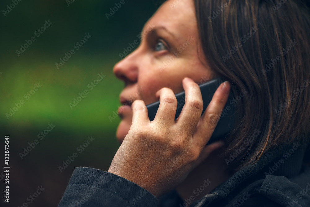 Woman with serious face expression talking on phone in park Woman with serious face expression talking on phone in park