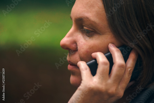 Woman with serious face expression talking on phone in park