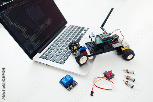 Diy rc car with components on laptop. Workplace of electronic inventor with constructed toy, wireless transceivers, servo and rey module near computer photo