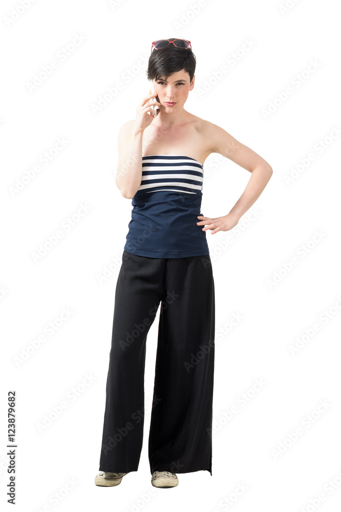 Serious stern woman in wide-leg pants talking on the phone looking at camera. Full body length portrait isolated over white studio background. Serious stern woman in wide-leg pants talking on the phone looking at camera. Full body length portrait isolated over white studio background.