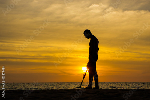 Treasure hunter with Metal detector on the sunset the beach