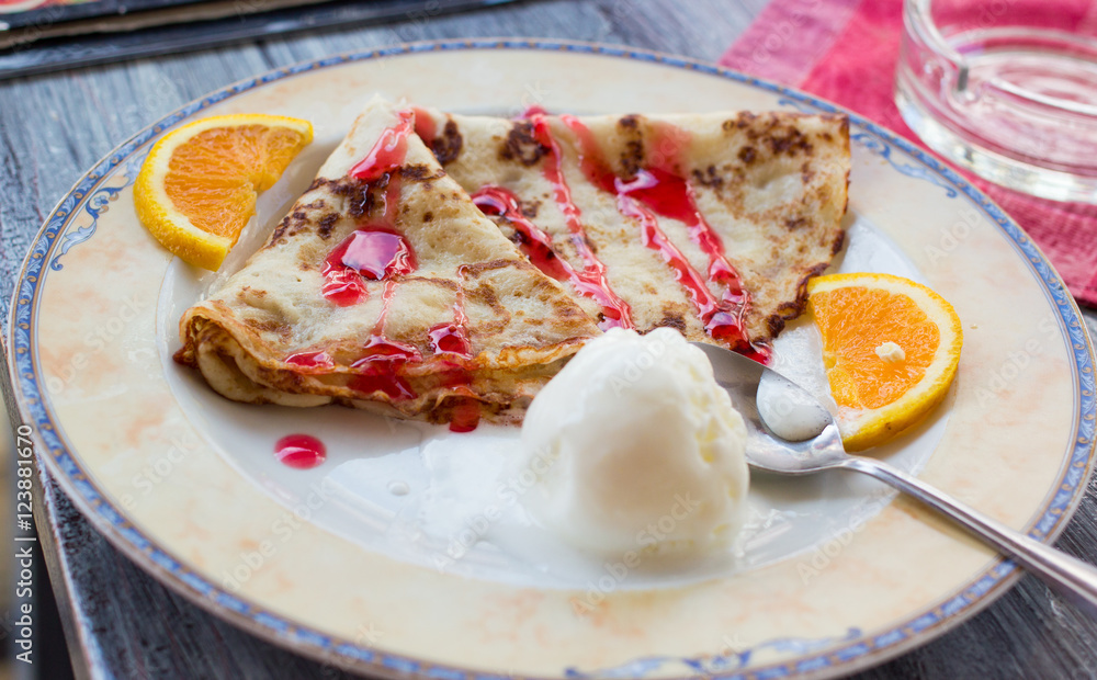 closeup shot of a dish plate with fritters pancakes, ice-cream ball, red topping, slices of orange and spoon