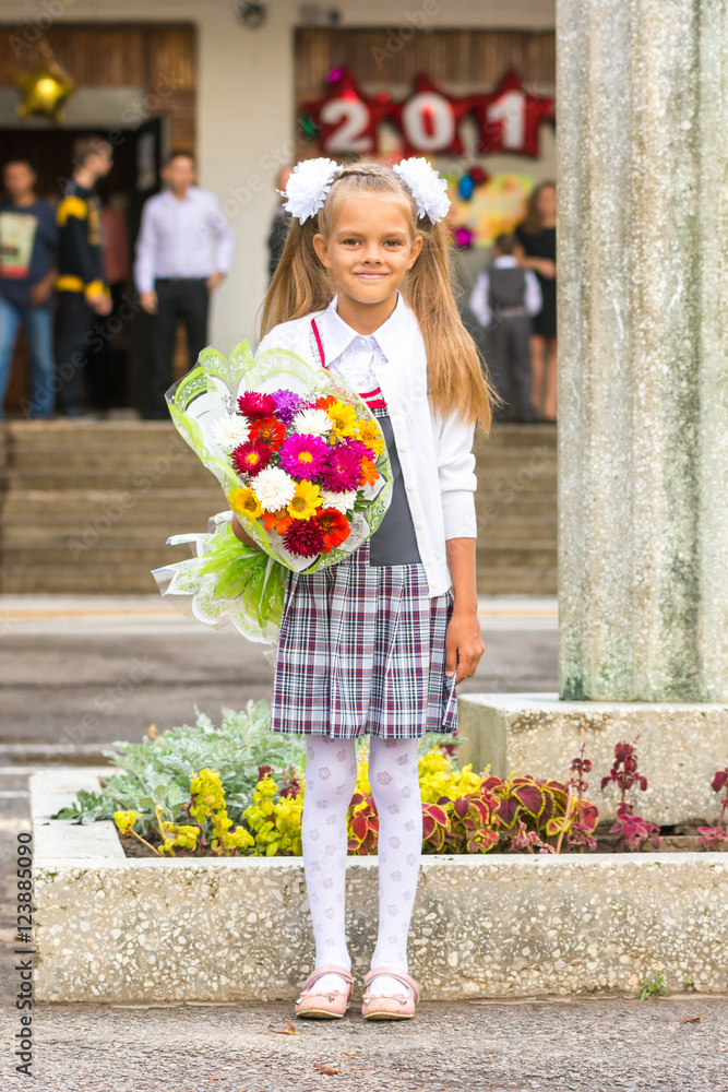 Fototapeta premium Grower Baby girl first-grader with a bouquet of flowers at the school