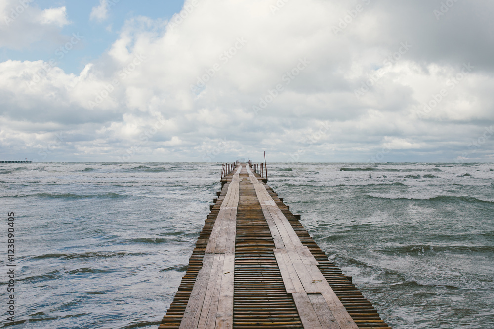 Perspective view of a wooden pier on the seashore with stormy sea