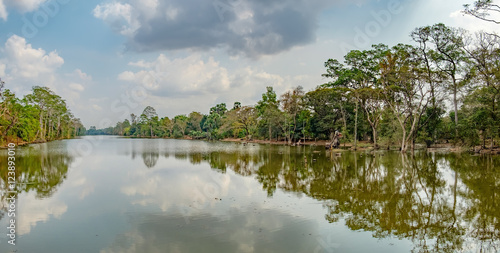 Beautiful lake nestled among rainforest in Cambodia under blue sky with white clouds. It surrounding mysterious ruins of Angkor Thom in Siem Reap, Cambodia.