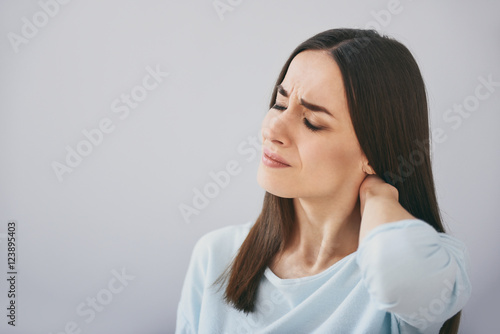 Pretty exhausted woman closing eyes and standing against white wall.