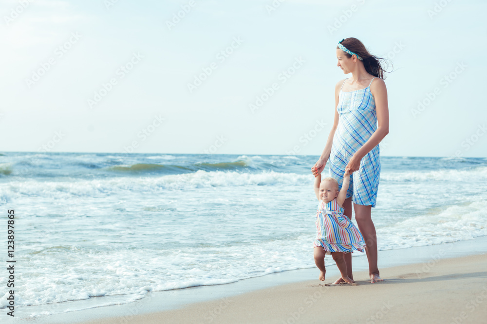 Mother and daughter walking on the beach. Mom teaches daughter to make first steps Mother and daughter walking on the beach. Mom teaches daughter to make first steps