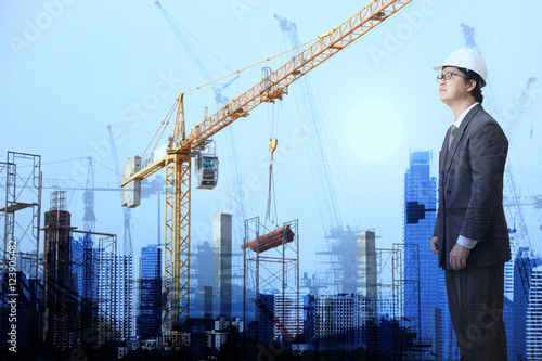 businessman with Crane and workers at construction site against blue sky.