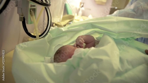 This tiny little baby has just been born. She is moving her hands a bit and is covered with blankets. A nurse is doing something in the background.
 photo