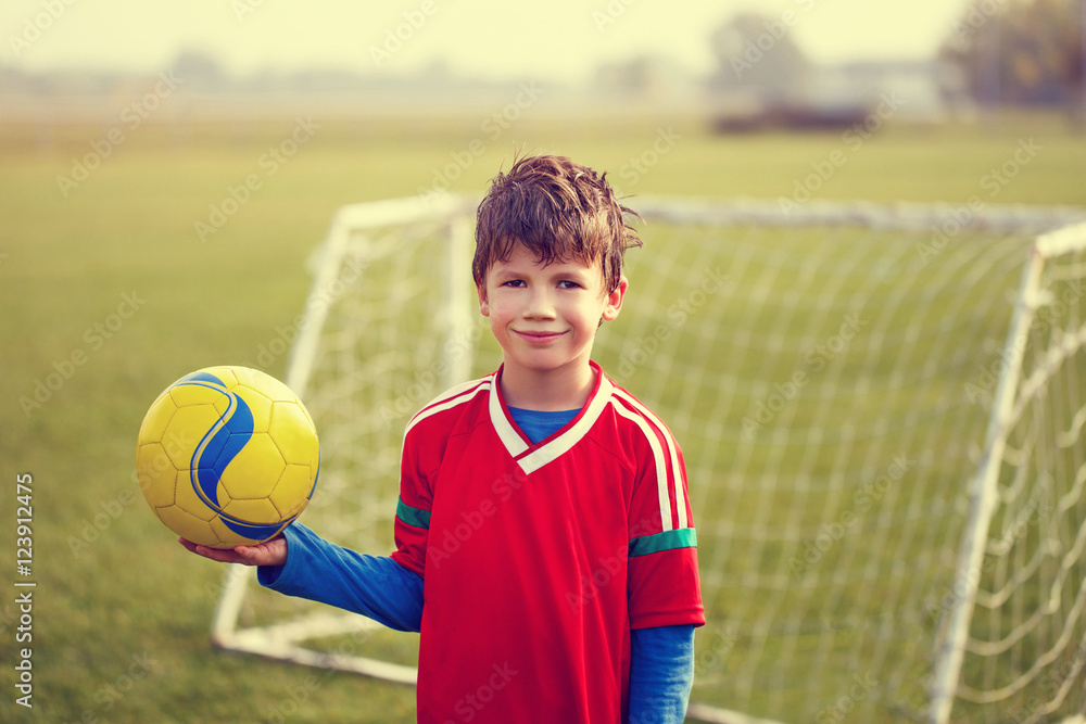 Happy young little boy holding soccer ball on field