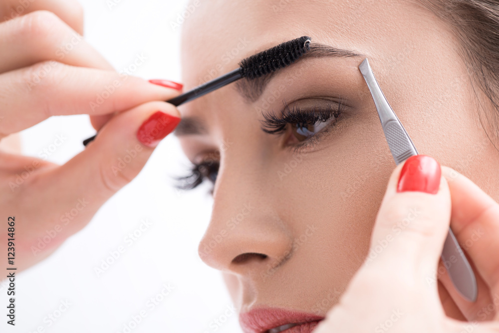 Young woman tweezing her eyebrows in beauty saloon