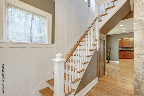 Staircase with white and brown railings and wood paneled walls