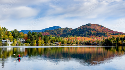 A panoramic view of Mirror Lake in Lake Placid  New York  on a sunny autumn day with colorful fall foliage on the mountains in the background